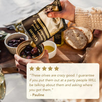 Hand holding a package of olives with a wooden cutting board and bread in the background, featuring a five-star rating and review.