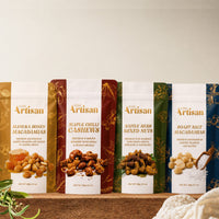 Assorted packages of 'Kiwi Artisan' nut products on a wooden surface with a neutral background.