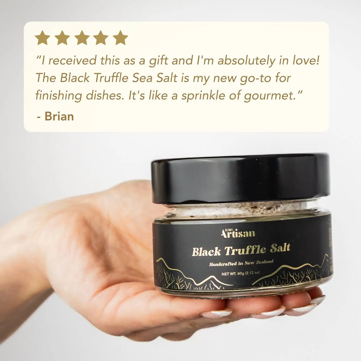 Hand holding a jar of Black Truffle Sea Salt with a customer review on a light gray background