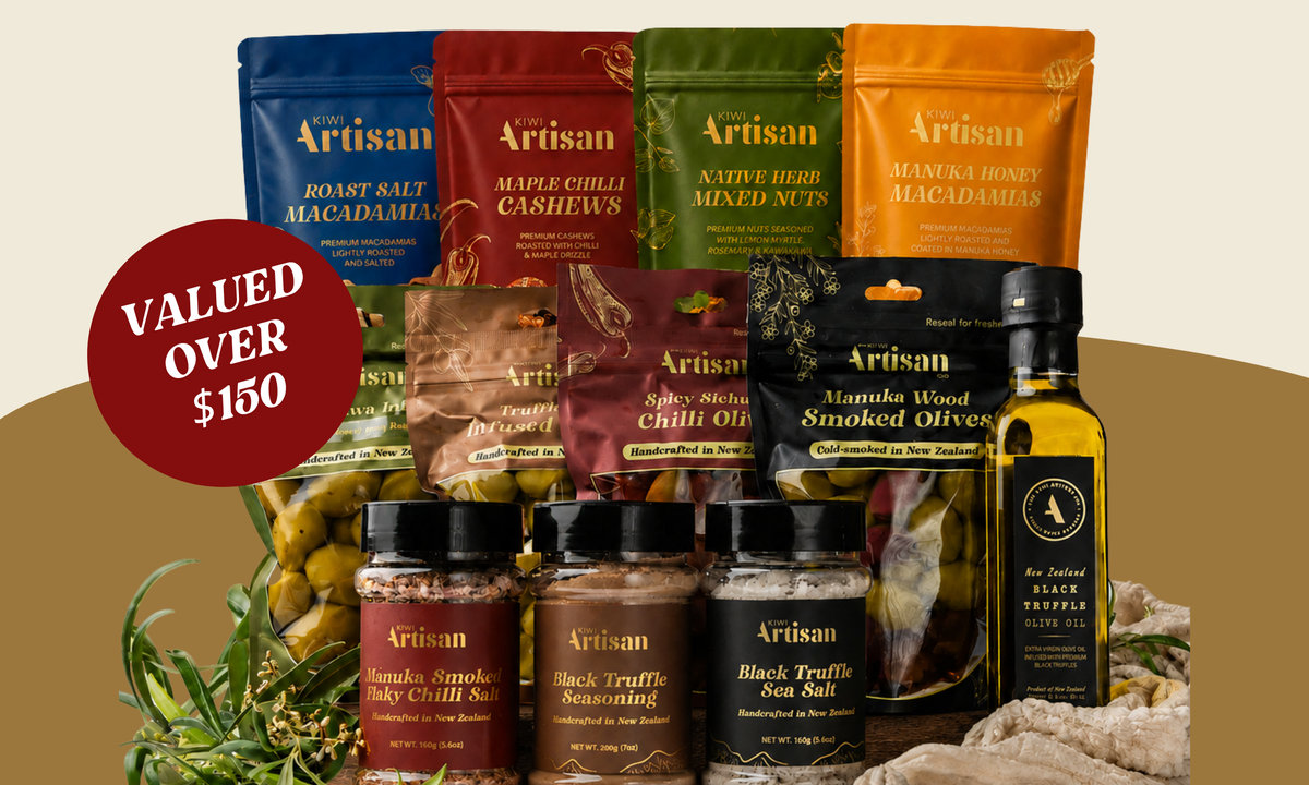 A curated olive oil and snack gift set from Artisan, featuring multiple colorful pouches of macadamia, cashew, and nut spreads, jars of black truffle salt and smoked olive oil, and a bottle of black truffle oil arranged on a beige surface with a red 'VALUED OVER $150' badge.