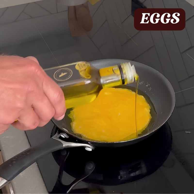 Person pouring truffle oil onto a frying pan with an egg cooking on a stove.