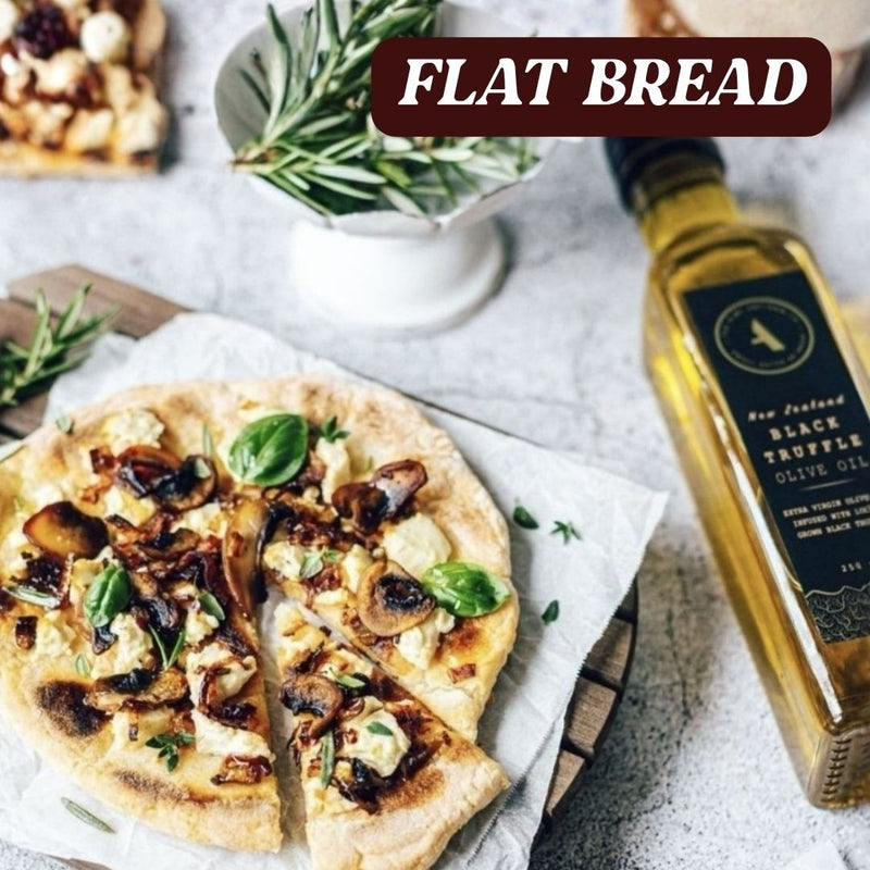 Flatbread with toppings on a wooden board with a bottle of black truffle  olive oil and rosemary in the background.